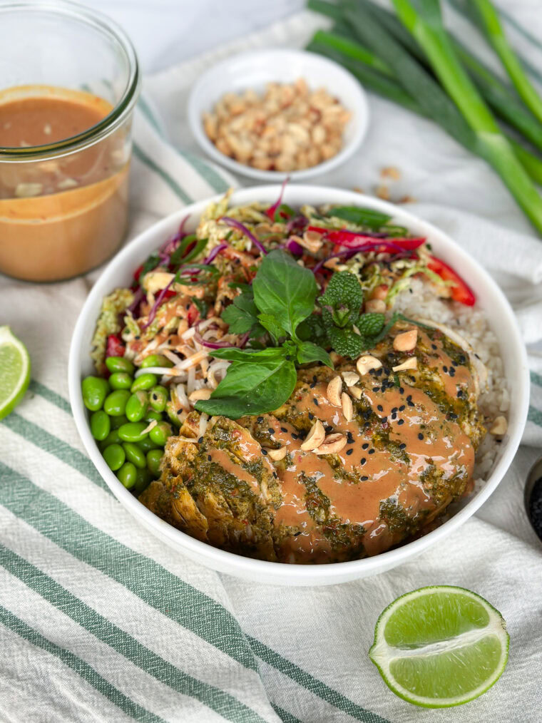 a ceramic bowl with edamame, cilantro, chicken, cabbage, with peanut sauce drizzled on top