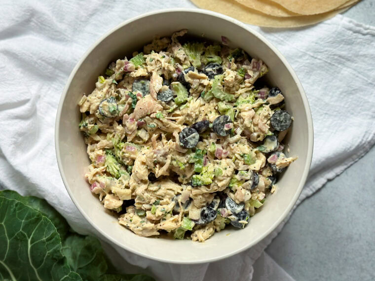 flat lay of a bowl of combined shredded chicken, chopped celery, red onions, grapes, collard greens, homemade honey mustard dressing, and herbs for the Honey Mustard Chicken Salad Wrap