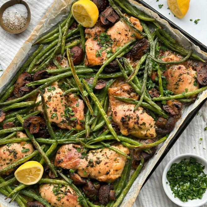 a sheet pan with freshly cooked butter, garlic chicken thighs, and lemon wedges.