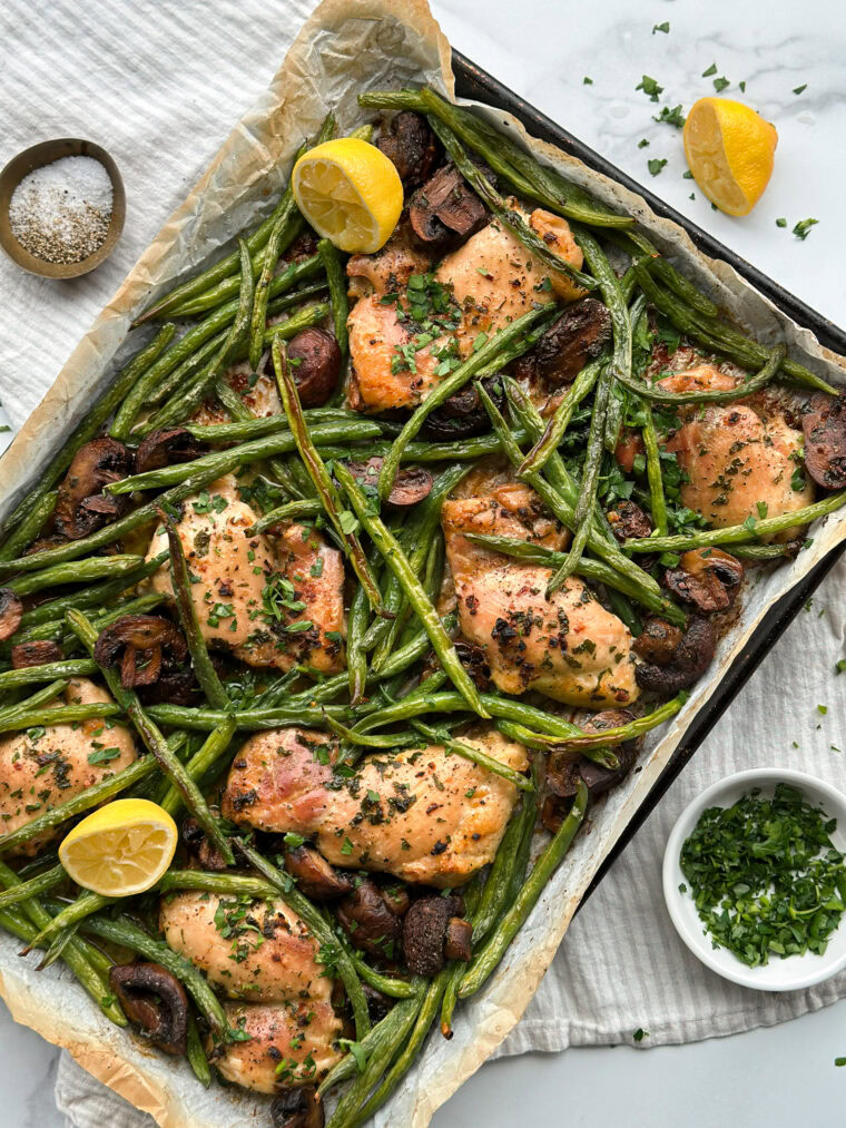 a sheet pan with freshly cooked butter, garlic chicken thighs, and lemon wedges.