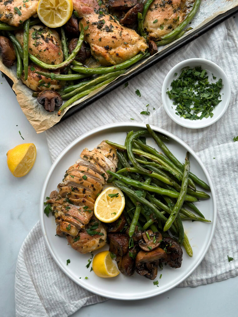 a white ceramic plate with butter garlic chicken thighs, green beans, and a lemon slice on top
