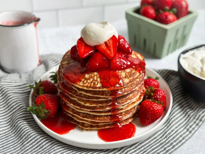 Horizontal shot of pancake stack topped with coconut cream and strawberries
